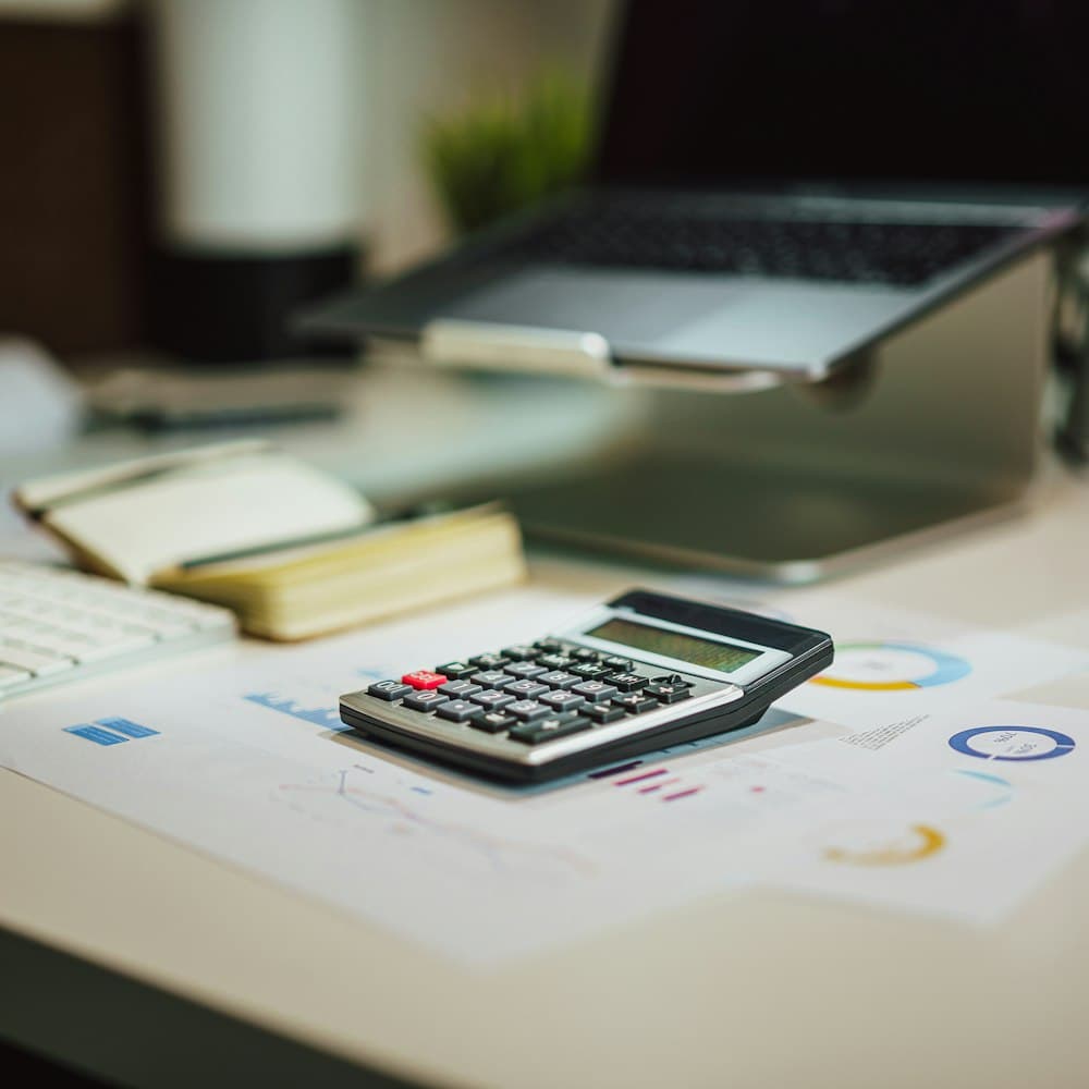 Calculator and printed reports on a desk beside a laptop